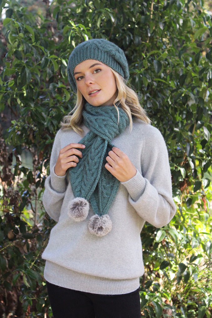 This chunky cable knit scarf with Rabbit fur pom poms, in contrasting colours, is soft and warm. Colour - sage with grey pom poms.