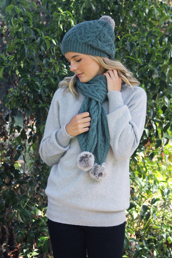 A relaxed cable beaine with rabbit fur pom pom. Colour - Sage with grey pom pom.