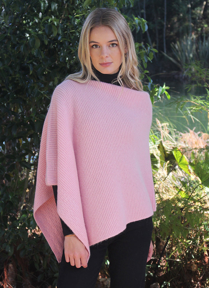 This asymmetrical poncho is a rib knit which also has a textured detail on one side. Soft, warm and available in five colours. Made in NZ by Lothlorian. Rose.