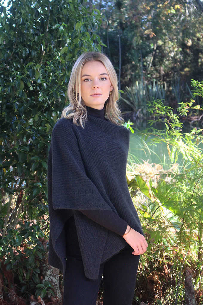 This asymmetrical poncho is a rib knit which also has a textured detail on one side. Soft, warm and available in five colours. Made in NZ by Lothlorian. Slate. 