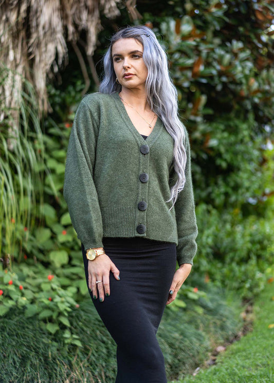 A modern twist on a V neck cardigan. This style is hip length and features oversize two tone buttons and a wide rib detail on the hem. In the beautiful new Koru shade of Moss. Includes a spare button. Made in NZ by Koru.  Moss.